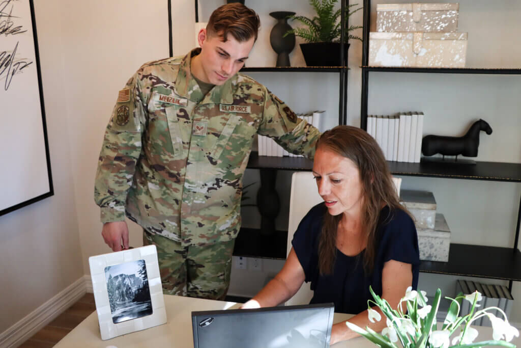 A military relocation professional is helping a uniformed soldier review new home listings on a computer